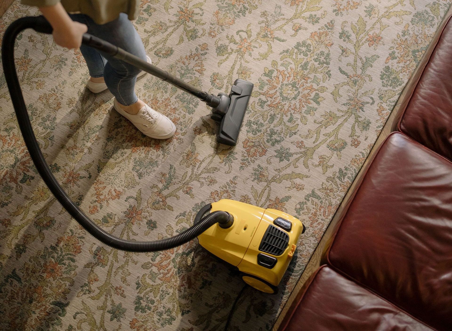 Overhead view of a woman vacuuming a carpet at home, highlighting cleanliness and housekeeping.